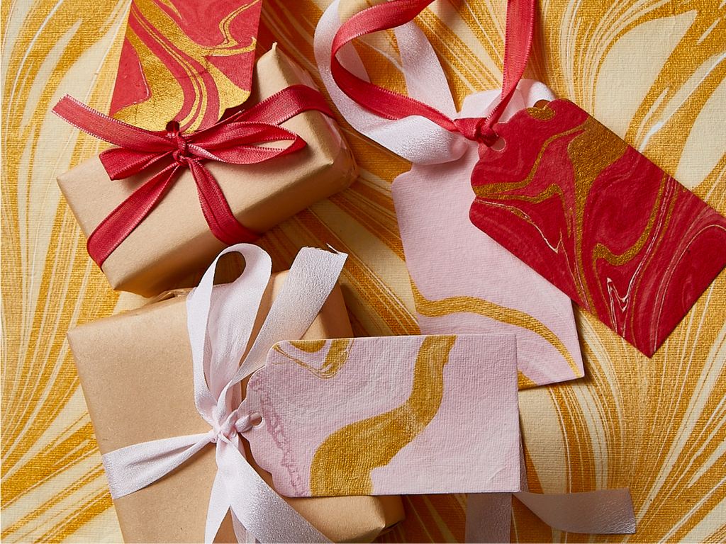 A gold and cream swirly backdrop featuring brown paper-wrapped gifts, red and white ribbons, and gift tags.