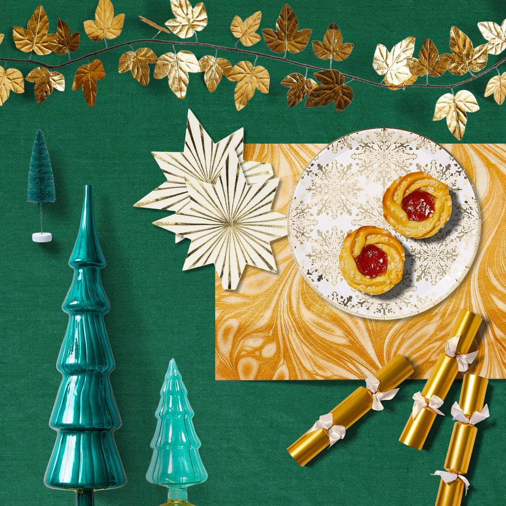 Decorative Christmas trees, gold party crackers, gold garland, and a plate with holiday pastries arranged on a green backdrop. 